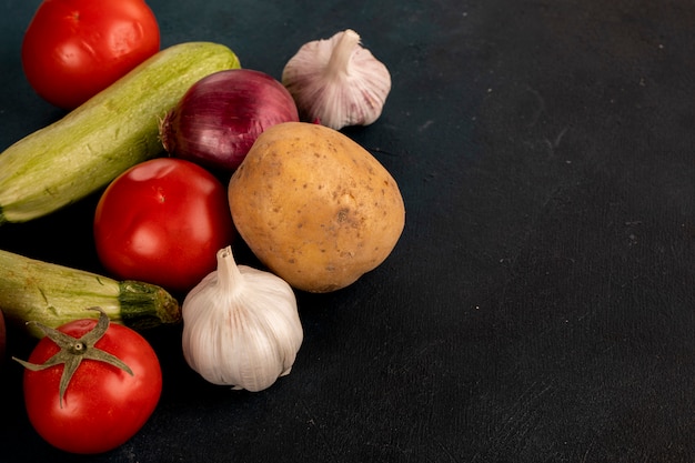 Mischgemüse einschließlich Knoblauchhandschuhe, Kartoffeln, Zwiebel, Zucchini und Tomaten auf schwarzer Tabelle.