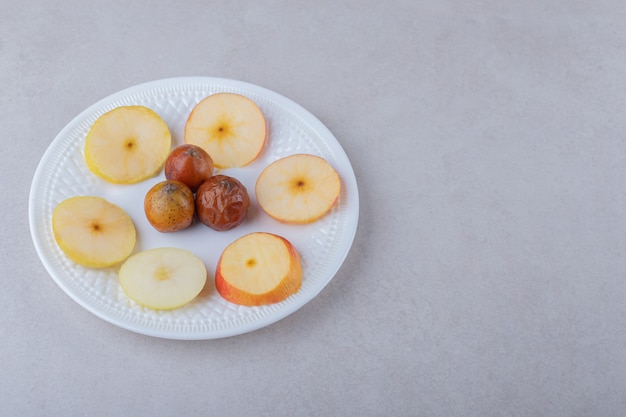 Mispel und geschnittene Äpfel auf Teller auf Marmortisch.