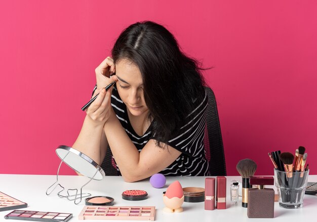 Mit Blick auf den Spiegel sitzt das junge schöne Mädchen am Tisch mit Make-up-Tools