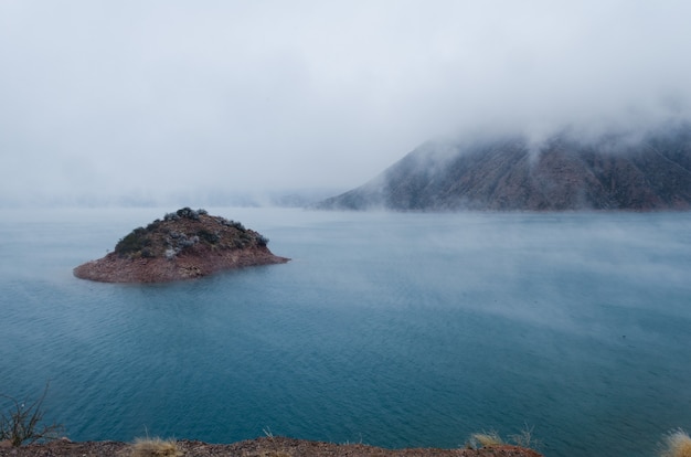 Mit Blick auf eine kleine Insel mit einem im Winter mit Nebel bedeckten Berg