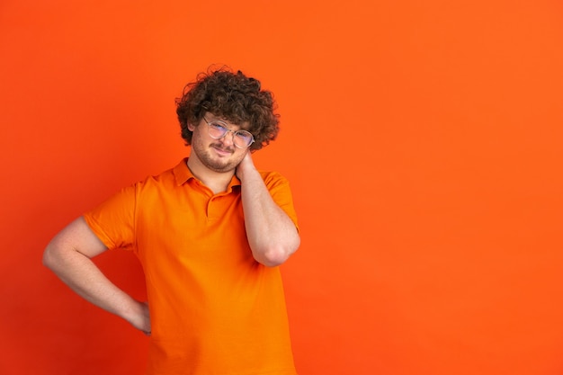 Mit etwas unzufrieden. Das monochrome Portrait des kaukasischen jungen Mannes auf oranger Wand. Schönes männliches lockiges Modell im lässigen Stil.