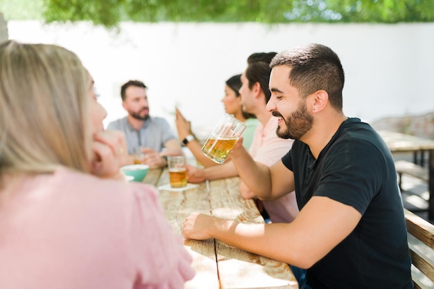 Mit Freunden scherzen und lachen. Gut aussehender hispanischer Mann, der ein kaltes Bier trinkt und sich mit einer großen Gruppe von Freunden in einer Bar entspannt