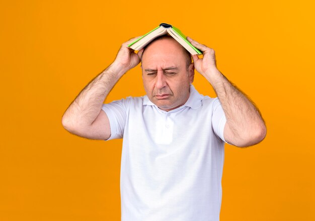 Mit geschlossenen Augen bedeckte trauriger lässiger reifer Mann bedeckten Kopf mit Buch, das auf gelber Wand lokalisiert wird