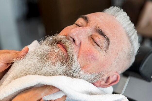 Mit Handtuch auf Bart des gealterten Mannes im Friseursalon