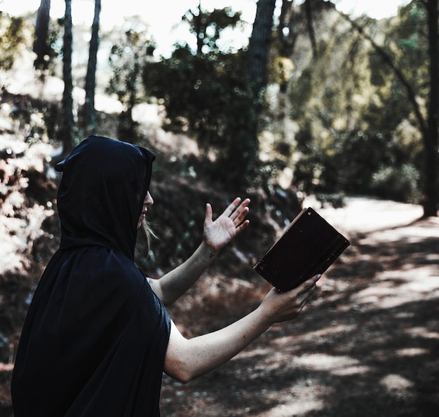 Mit Kapuze Frau mit dem Buch, das im sunlit Waldland beschwört