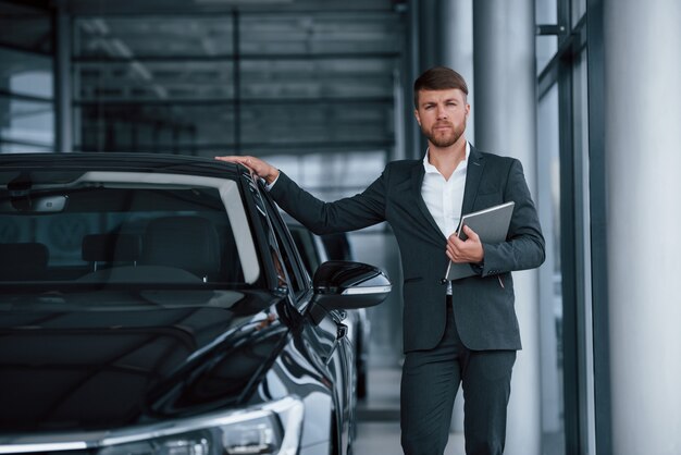 Mit silbernem Notizblock in der Hand. Moderner stilvoller bärtiger Geschäftsmann in der Automobillimousine