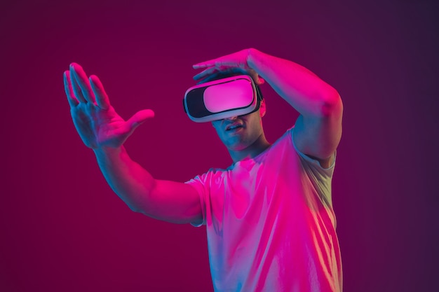 Mit VR spielen, filmen, fahren. Porträt des kaukasischen Mannes isoliert auf rosa-violetter Studiowand.