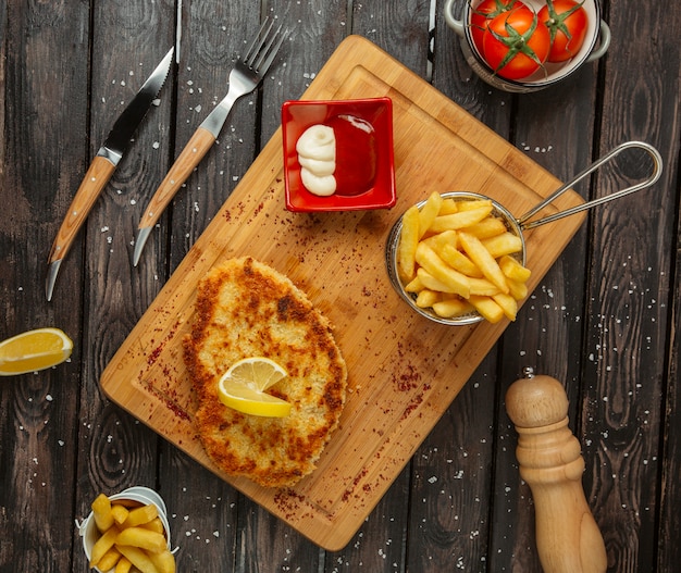 Mit Zitrone garnierte Hähnchenbrustpastetchen, serviert mit Pommes Frites, Mayonnaise und Ketchup