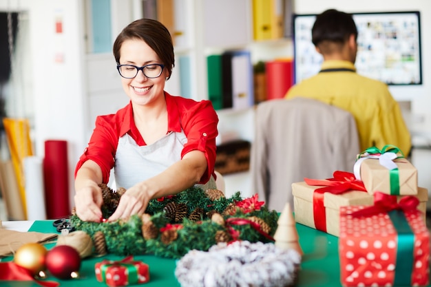 Mitarbeiter, der einen Weihnachtskranz macht und Geschenkboxen einwickelt