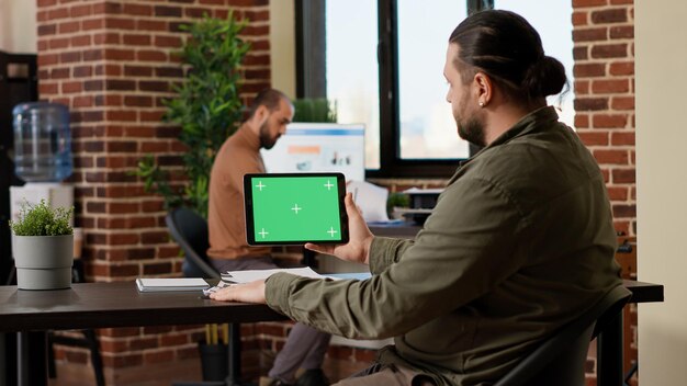 Mitarbeiter des Unternehmens betrachten Tablet mit horizontalem Greenscreen auf dem Display, arbeiten im Geschäft mit Chroma-Key-Hintergrund und isolierter Copyspace-Vorlage. Leerer Mockup-Bildschirm im Büro.