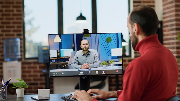 Mitarbeiter des Unternehmens, der eine Online-Videoanrufkonferenz nutzt, um sich im Büro aus der Ferne zu unterhalten. Männlicher Arbeiter, der mit einem Berater per Videokonferenz spricht und an einem Briefing-Meeting am Computer teilnimmt.