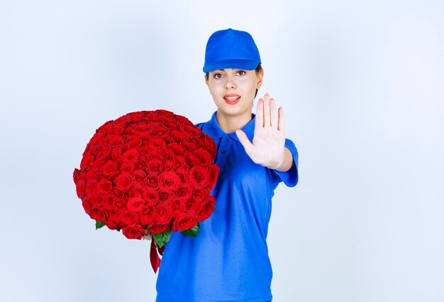 Mitarbeiterin der Lieferung in Uniform mit Rosenstrauß, die Stoppschild zeigt.