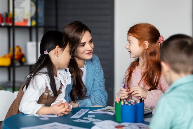 Mittelgroße Kinder, die mit dem Lehrer am Tisch sitzen