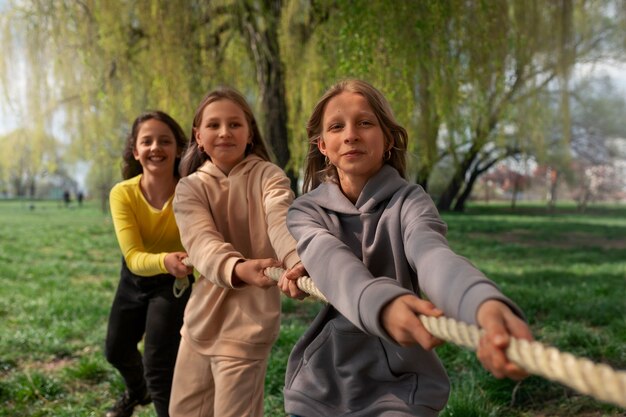 Mittelgroße Kinder spielen im Park Tauziehen