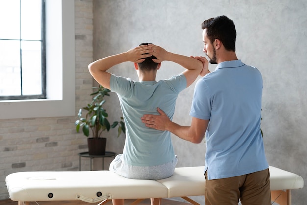 Kostenloses Foto mittelgroßer mann, der patienten in der physiotherapie hilft