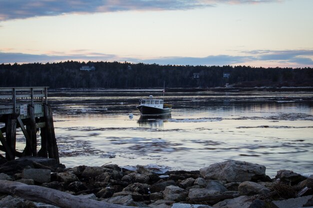 Mittelgroßes Fischerboot, das vor der Dämmerung am Ufer im Meer nahe einem felsigen Strand kreuzt