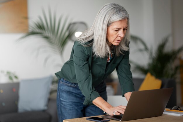 Mittlere Aufnahme alte Frau, die drinnen am Laptop arbeitet