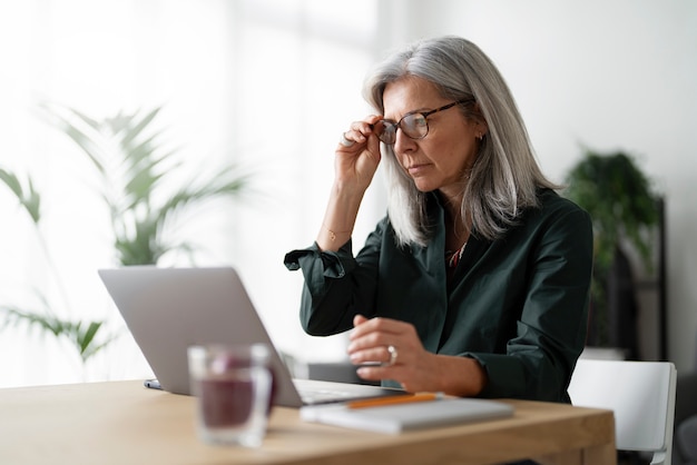 Mittlere Aufnahme alte Frau, die innen am Laptop arbeitet