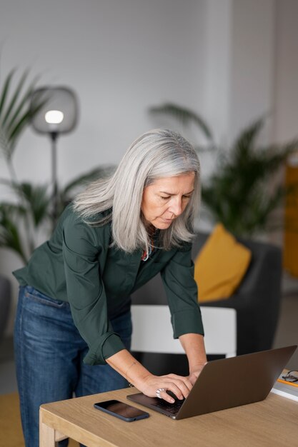 Mittlere Aufnahme alte Frau, die zu Hause am Laptop arbeitet
