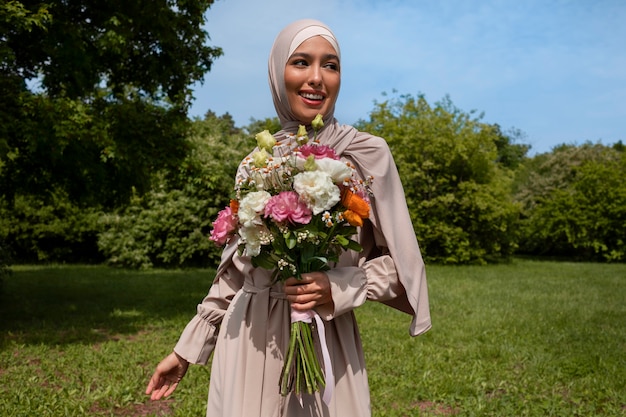 Mittlere Aufnahme einer muslimischen Frau, die mit Blumen posiert