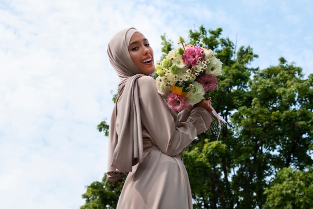 Mittlere Aufnahme einer muslimischen Frau, die mit Blumen posiert