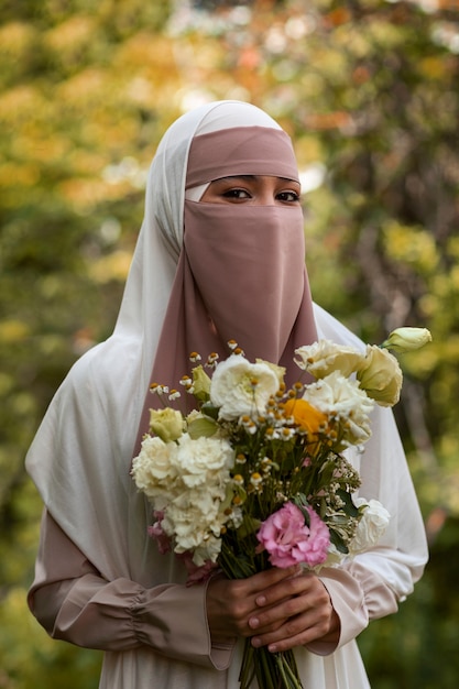 Mittlere Aufnahme einer muslimischen Frau, die mit Blumen posiert