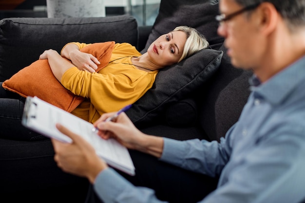 Mittlere erwachsene Frau, die sich während eines Termins mit ihrem Psychiater auf das Sofa legt