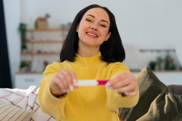 Mittlere schuss glückliche frau, die schwangerschaftstest hält