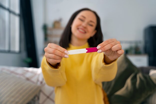 Mittlere schuss glückliche frau, die schwangerschaftstest hält