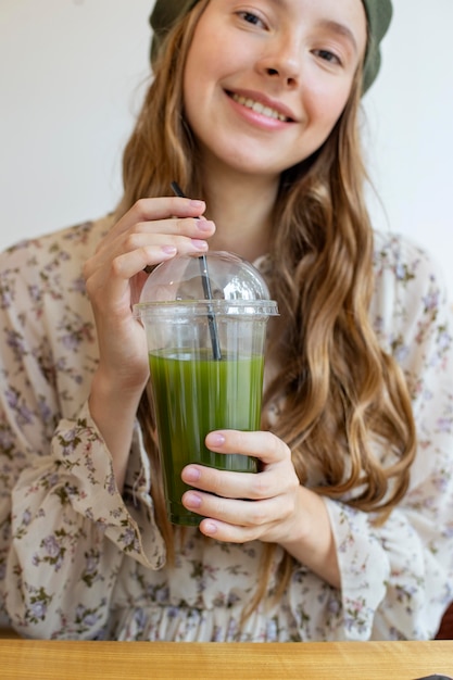 Mittlere Schussfrau, die am Tisch sitzt und Smoothie hält