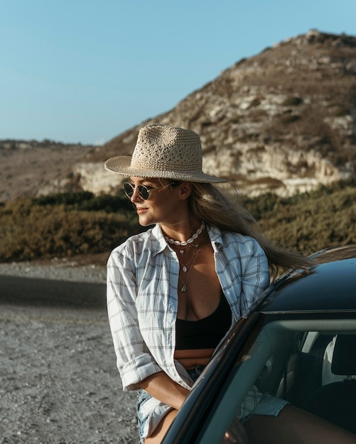 Kostenloses Foto mittlere schussfrau, die aus autofenster am strand steht