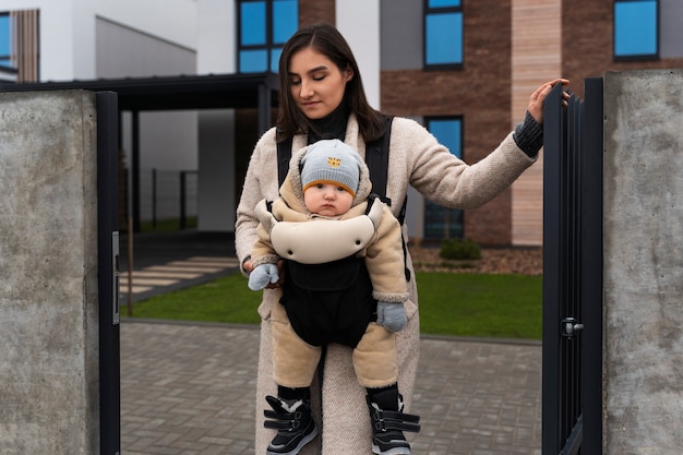 Kostenloses Foto mittlere schussfrau, die baby in träger hält