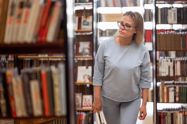 Kostenloses Foto mittlere schussfrau, die in bibliothek geht