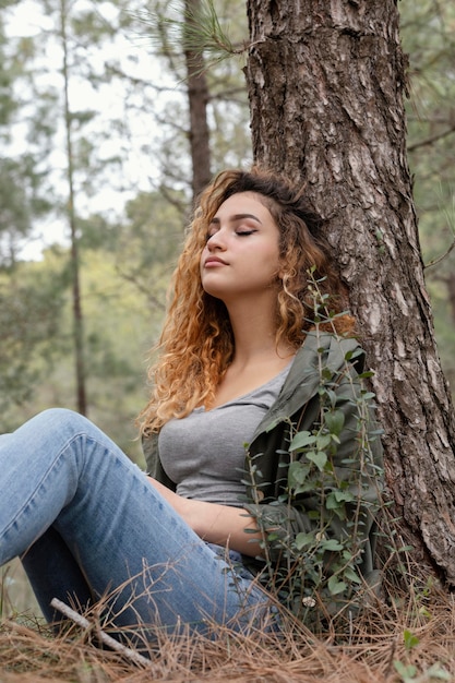 Kostenloses Foto mittlere schussfrau, die nahe baum sitzt