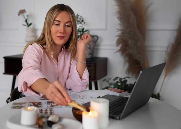 Kostenloses Foto mittlere schussfrau, die tarot mit laptop liest