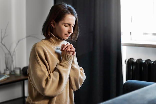 Kostenloses Foto mittlere schussfrau, die zu hause betet