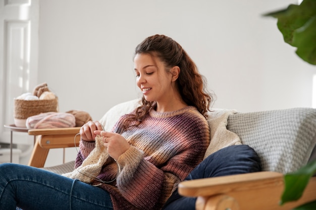 Kostenloses Foto mittlere schussfrau, die zu hause strickt