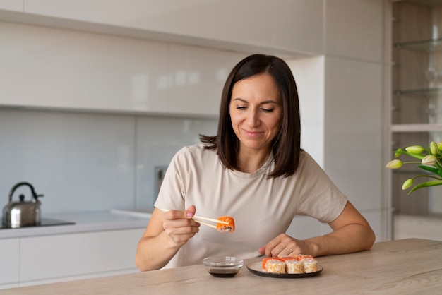 Kostenloses Foto mittlere schussfrau, die zu hause sushi isst