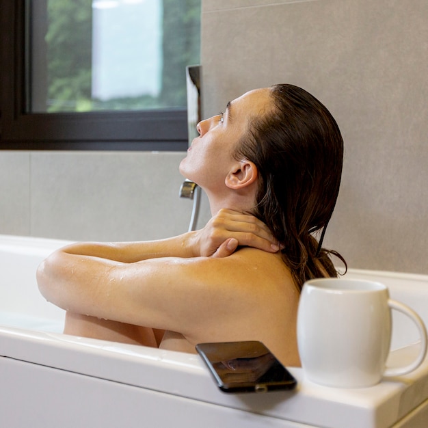 Mittlere Schussfrau in der Badewanne mit Smartphone