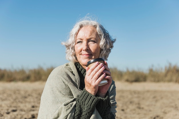 Kostenloses Foto mittlere schussfrau mit kaffee am strand