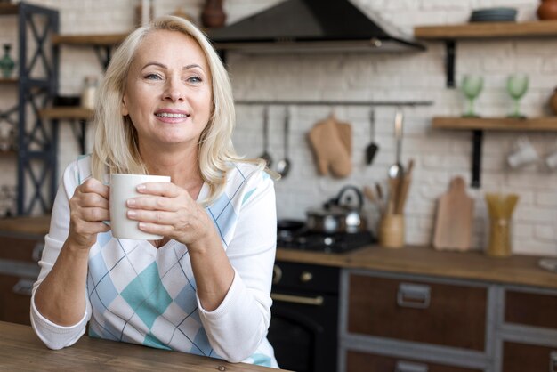 Mittlere Schussfrau mit Kaffeetasse in der Küche