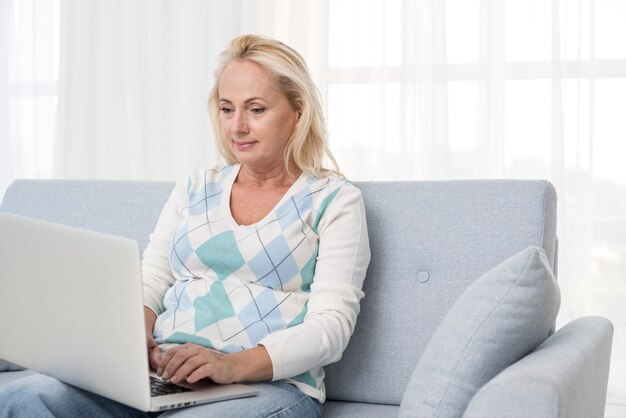 Mittlere Schussfrau mit Laptop auf der Couch