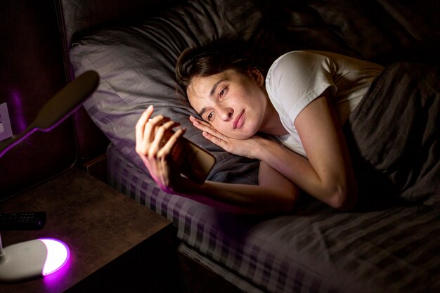 Mittlere Schussfrau mit Smartphone im Schlafzimmer