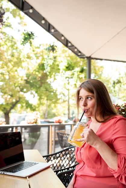 Mittlere Schussfrau mit trinkendem Saft des Laptops