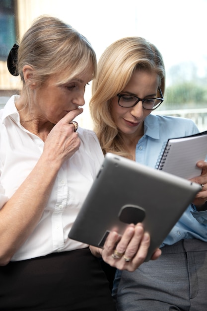 Mittlere Schussfrauen, die mit Tablette arbeiten