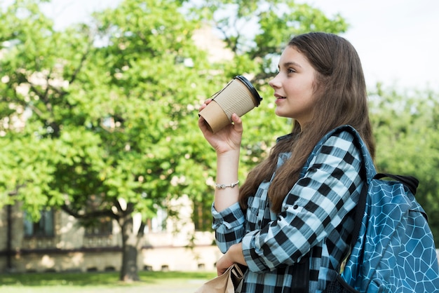 Mittlere Schussjugendliche der Seitenansicht, die vom papercup trinkt