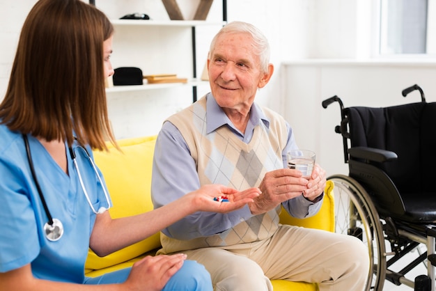 Mittlere Schusskrankenschwester, die einem alten Mann seine Pillen gibt