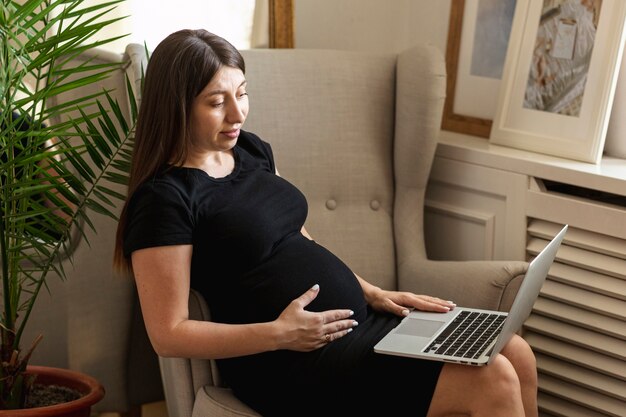 Mittlere schwangere Frau des Schusses, die ihren Laptop hält