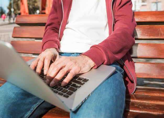 Mittlerer Abschnitt des Mannes sitzend auf der Holzbank, die auf Laptop schreibt