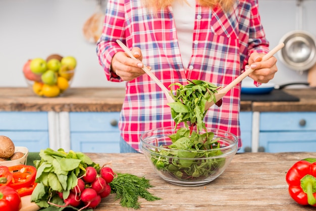 Mittlerer Abschnitt einer Frau, die belaubten Gemüsesalat mit hölzernem Löffel auf Holztisch hält